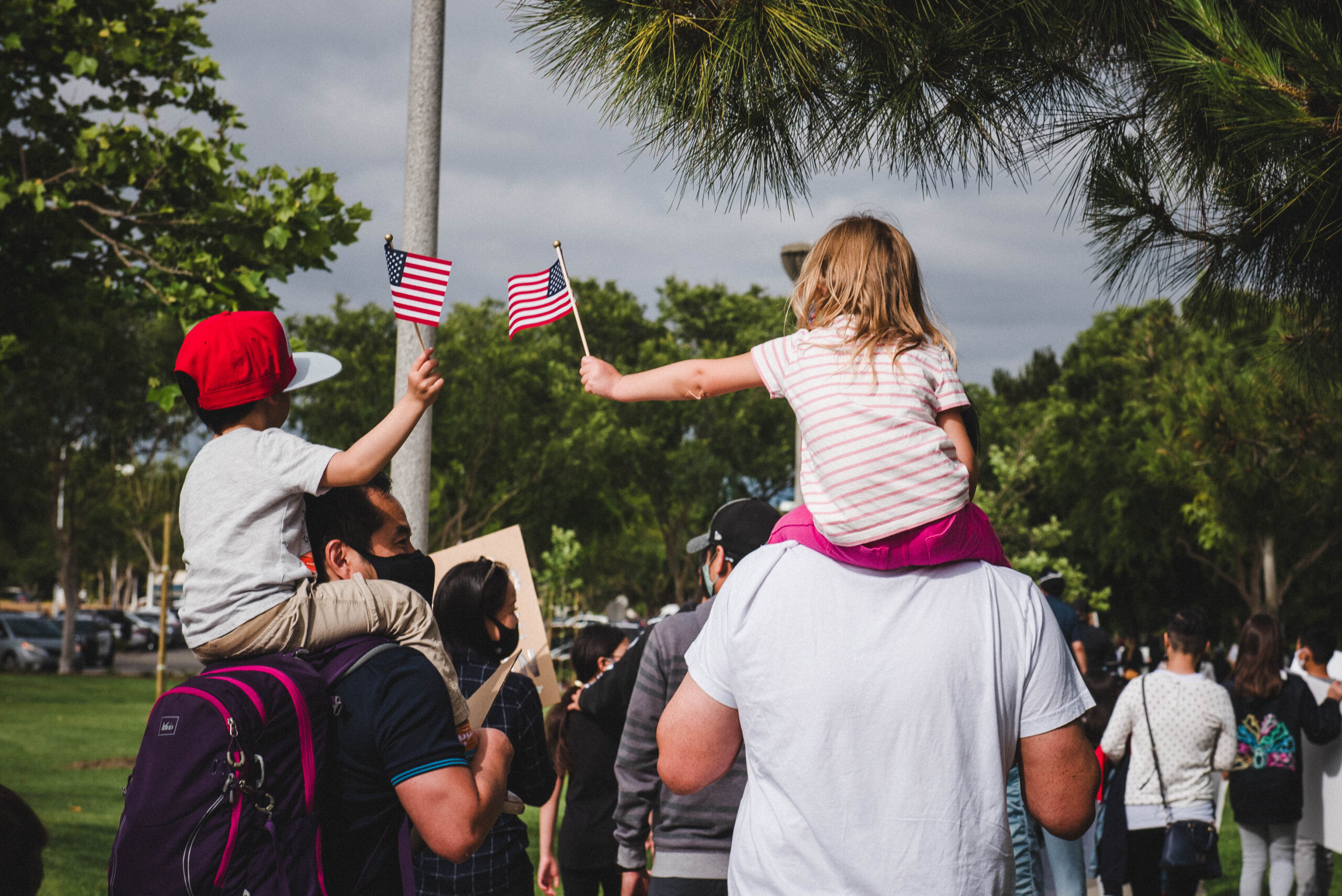 Two kids holding American flags and sitting on the shoulders of their parents.
